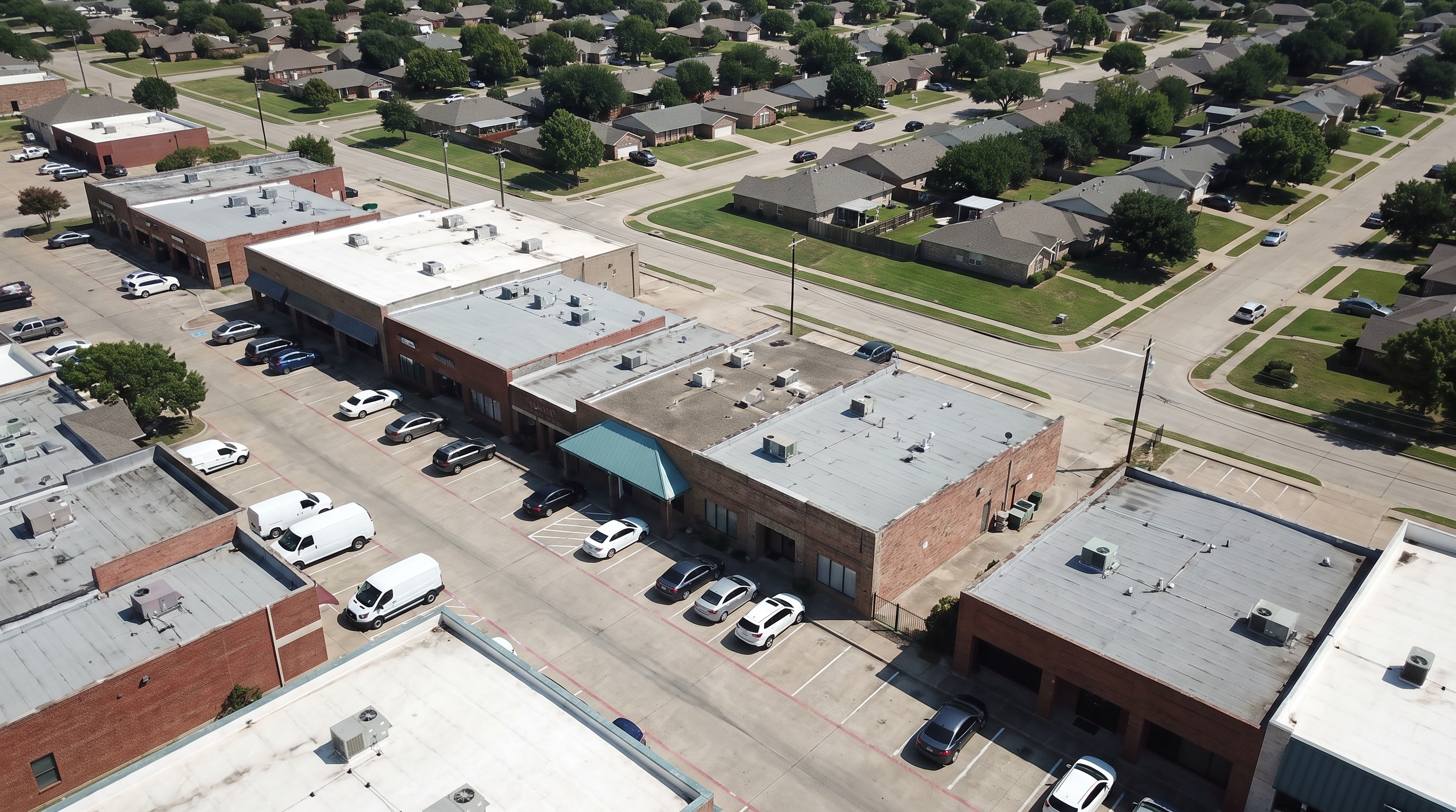 Aerial view of a suburban North Texas shopping strip with small businesses, parked cars and vans, and connecting streets running into nearby neighbourhoods.