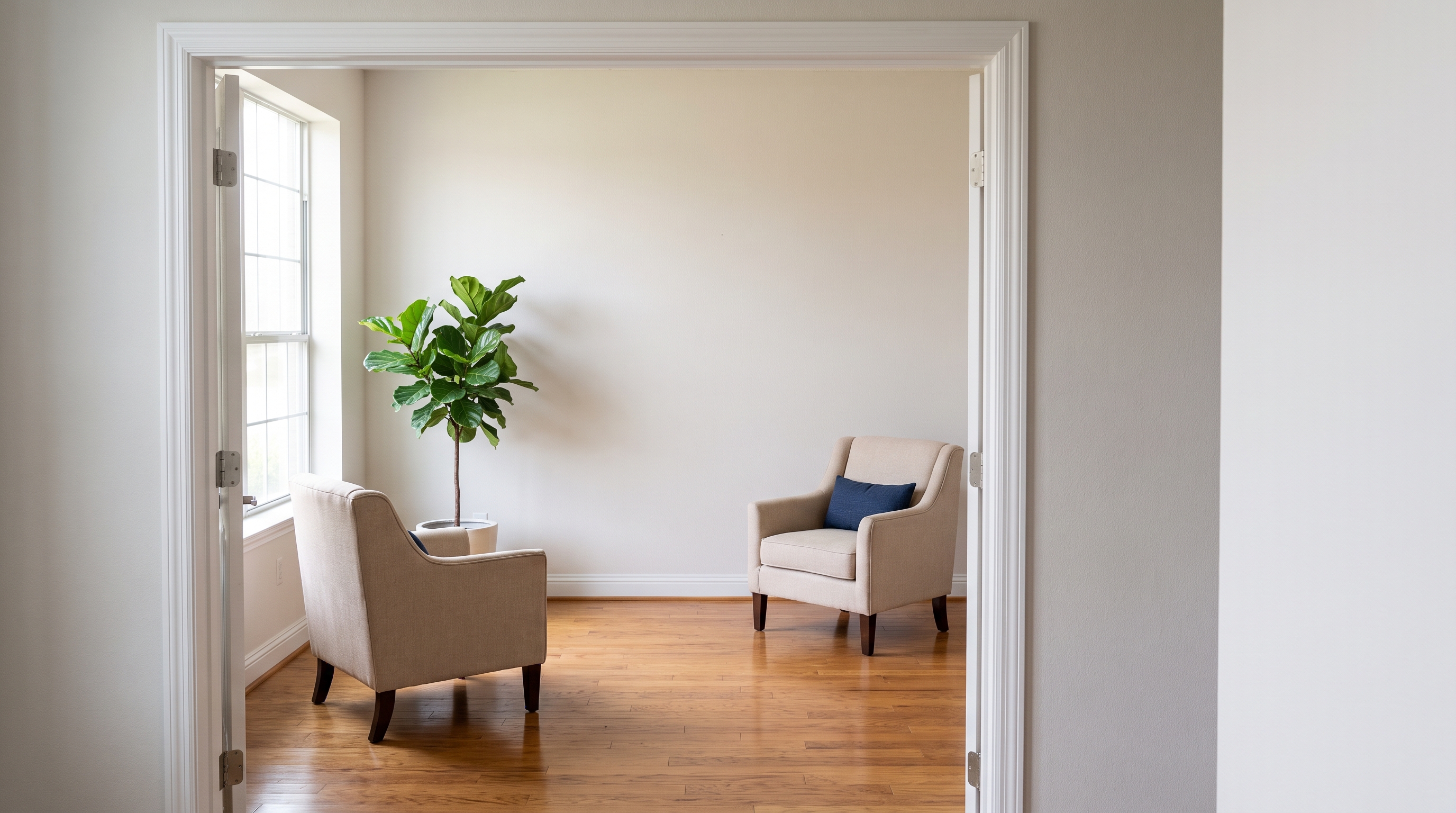 A sunlit, empty coaching studio seen through an open doorway, with two armchairs facing each other on a wood floor.